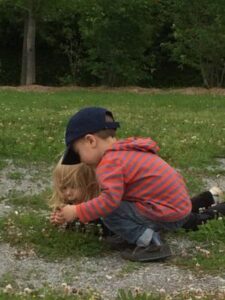 Toddler crouching beside friend while examining the ground.