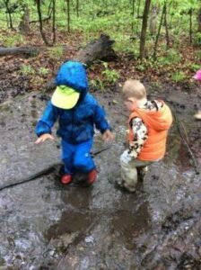Two children splashing in large muddy puddle in forest.