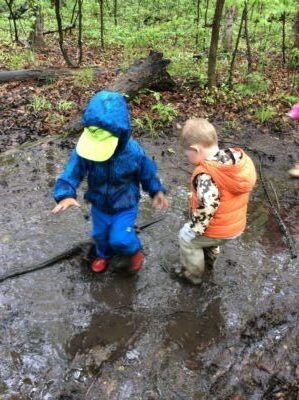 Two children splashing in large muddy puddle in forest.