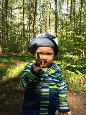 Child holding up muddy hand while smiling in the woods.