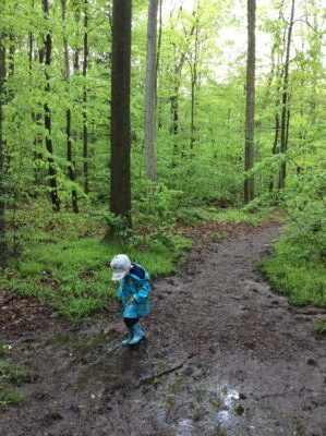 Child walking through a forest path covered in puddle.