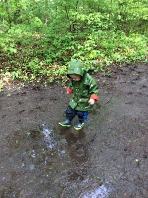 Child in a green raincoat stepping through mud in the woods.