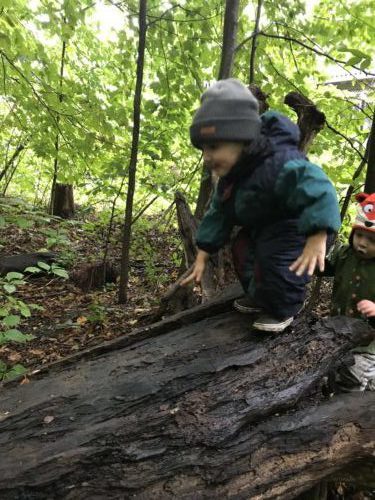 Child getting ready to leap off a mossy log during outdoor play.