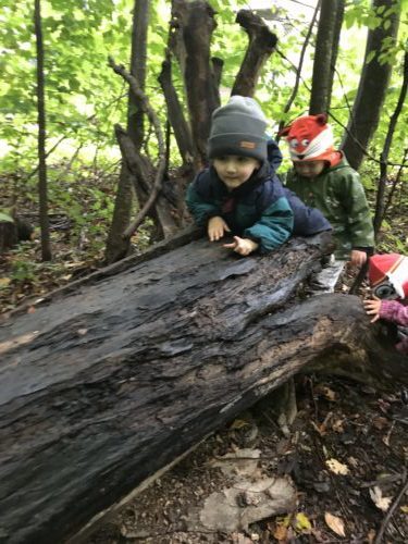 Child climbing up a slanted log with other children wait for their turn in a line behind him.