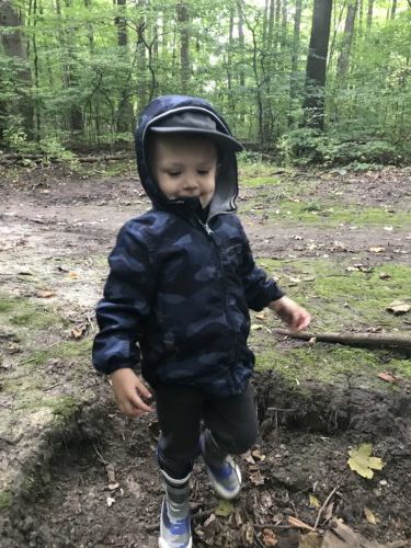 A young child stands happily in the forest, enjoying a moment of independent exploration.