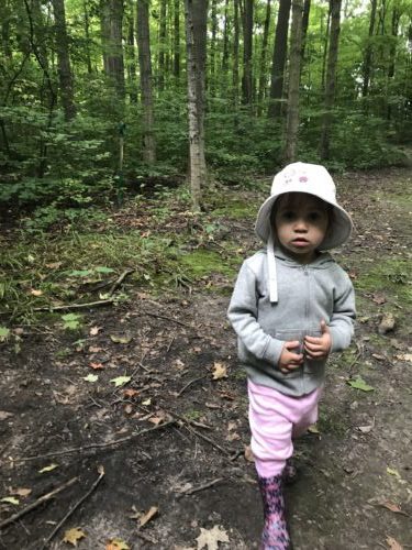 Toddler in light hoodie and pink pants walking on forest trail.