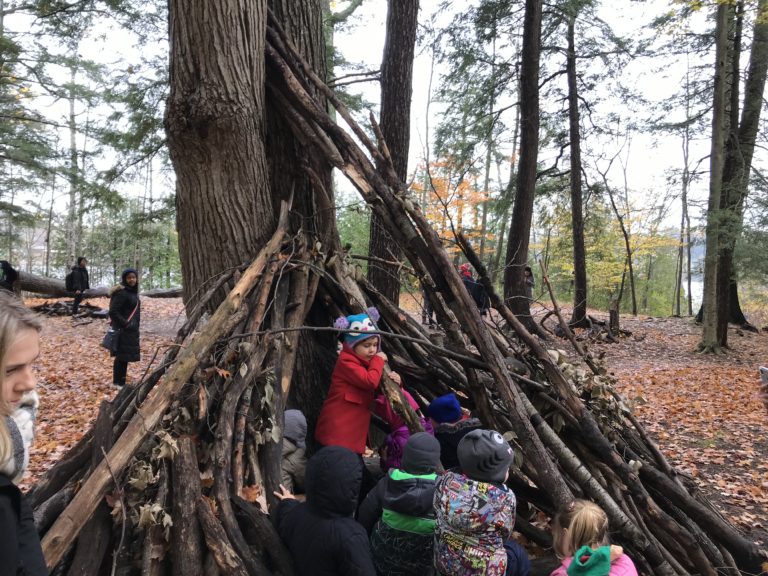 Children exploring a large wooden teepee-style structure built with branches.