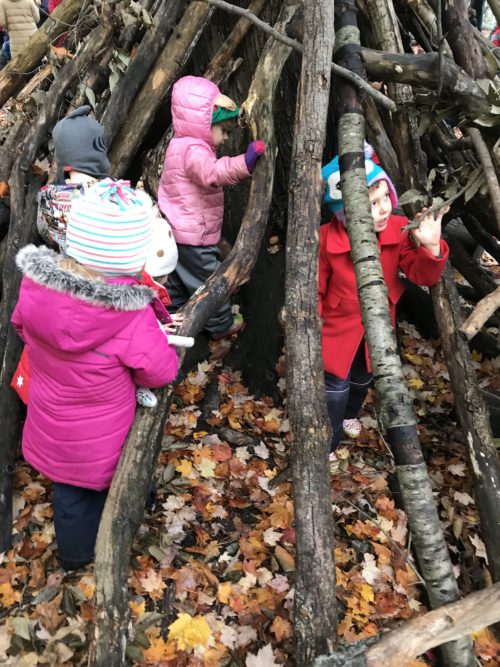 Children playing and exploring inside a large stick shelter in the forest.