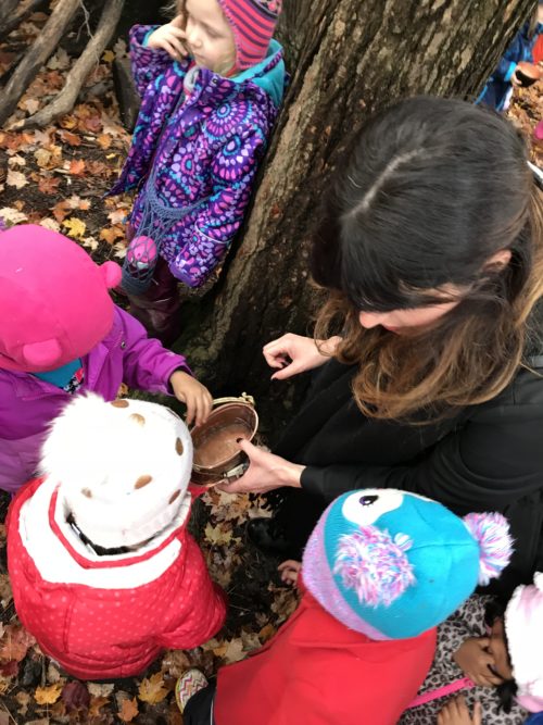 Educator showing a brass bowl to a group of children wearing colourful winter coats.