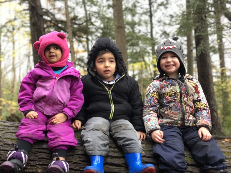Three children in jackets sitting on a fallen log in the forest.