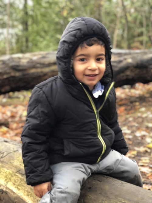 Young boy in a black jacket sitting on a log, smiling during the Indigenous water ceremony event.