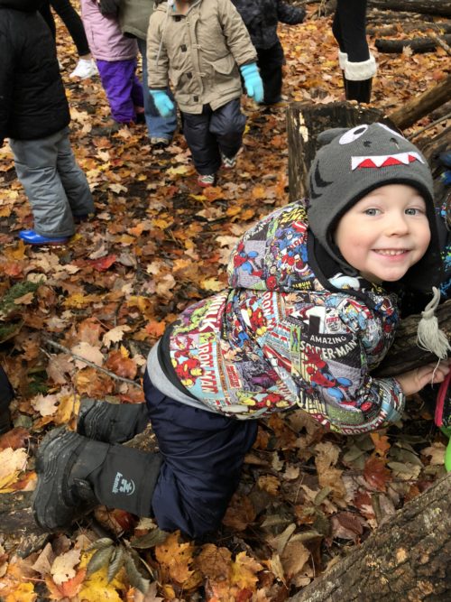 Smiling child in a patterned jacket and toque in the fall forest.