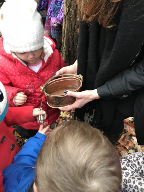 Close-up of children gathered around an educator holding a ceremonial brass bowl.