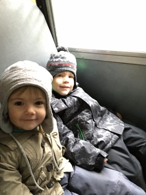 Two children bundled in winter jackets smiling during the bus ride.