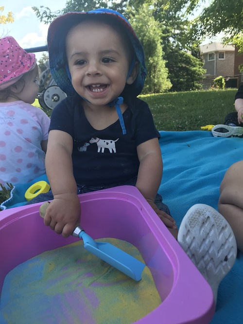 Smiling child scooping colourful sand from a pink bin.