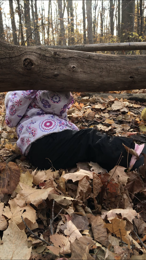 Child going under a log in a forest.