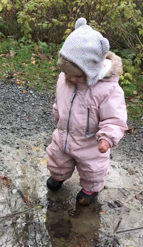 chilkd in white hat and pink snowsuit stepping in a puddle