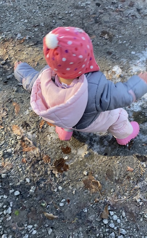 Child in pink hat stomping on puddles that have turned to ice