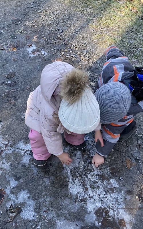 Two children pointing at frozen puddles on the ground