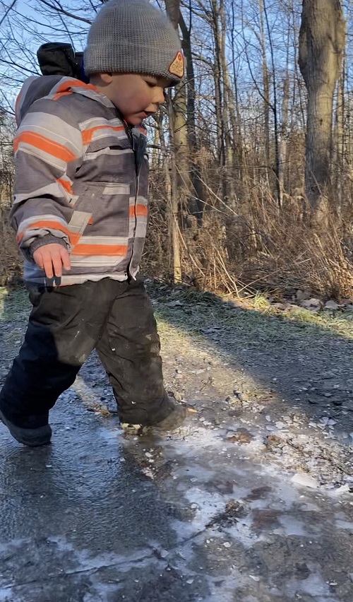 Child walking on puddles that have turned to ice, looking down