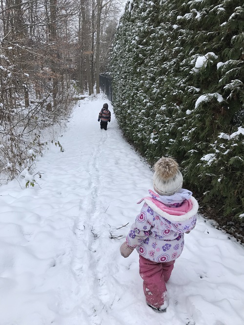 two children walking on a snowy forest trail