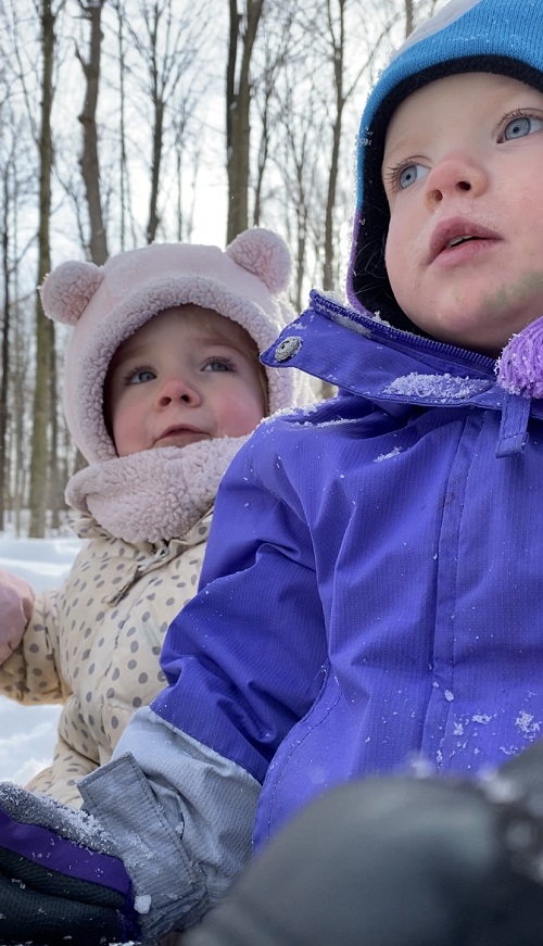 Two small children bundled up in a winter forest.