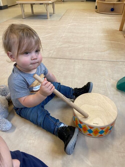 Child playing with a wooden drum during music time in the classroom.