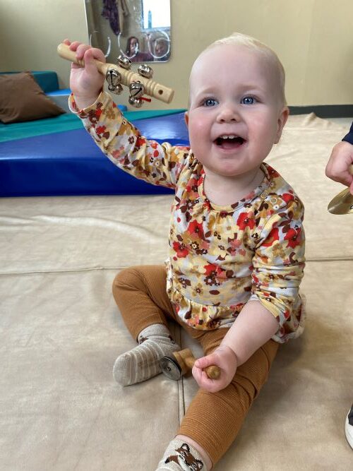 Little girl happily holding up a musical shaker.