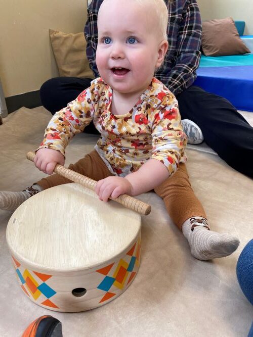 Happy little girl playing with a wooden drum.