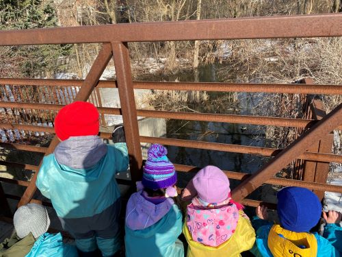 Children looking out from a metal bridge onto water.