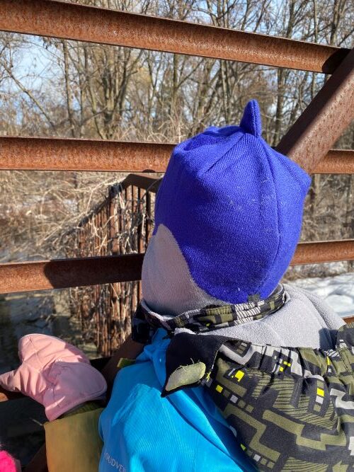 child in blue hat looking out from a bridge made of metal