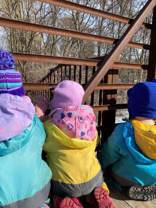 3 children looking out from a metal bridge.