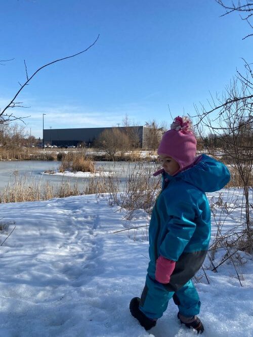 Boy standing in hat and jacket outside looking out at the snow and water.