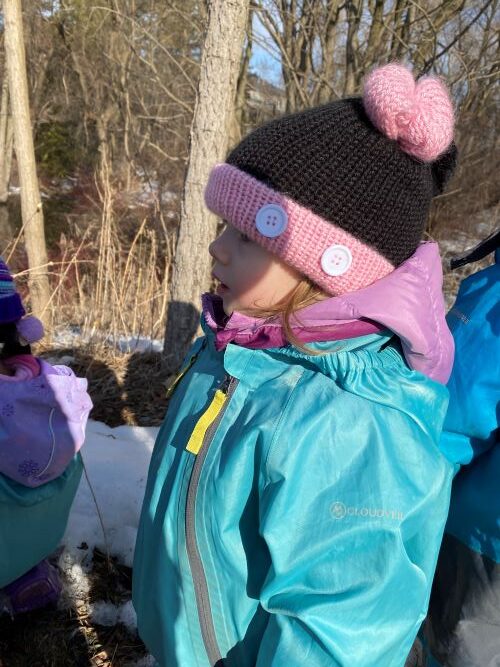 Child wearing pink and black hat and blue jacket outside