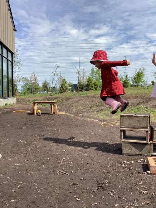 Girl mid-air with arms out jumping off a small wooden block.