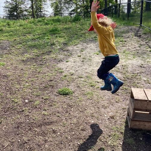 Boy mid-air jumping off a small wood block onto the ground.