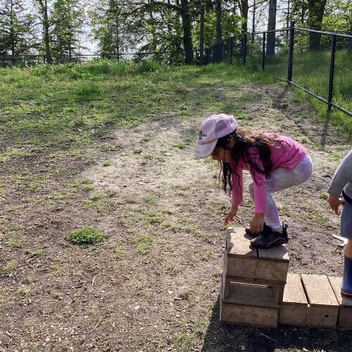 Girl about to jump off a small wooden block onto the ground.