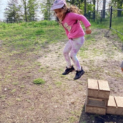 Girl mid-air jumping off a small wooden block onto the ground.