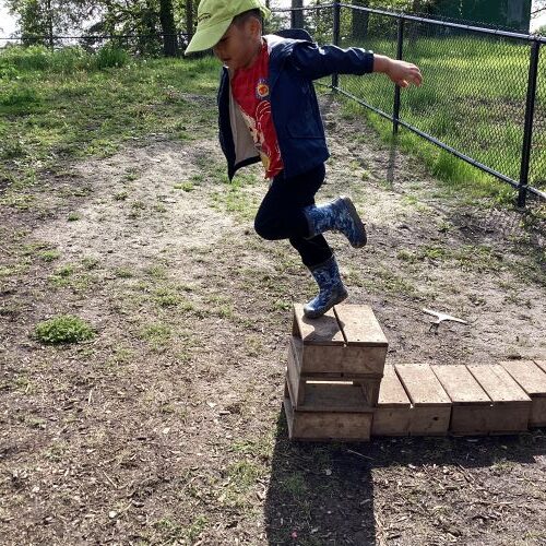 A preschool boy is about to jump off a small wooden block with arms out like he is learning to fly