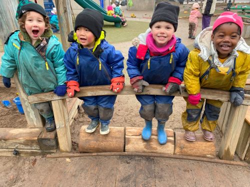 four children outside with jackets and hats posing for a photo