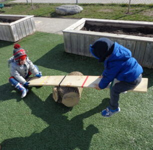 two kids on a wooden seesaw on artificial grass