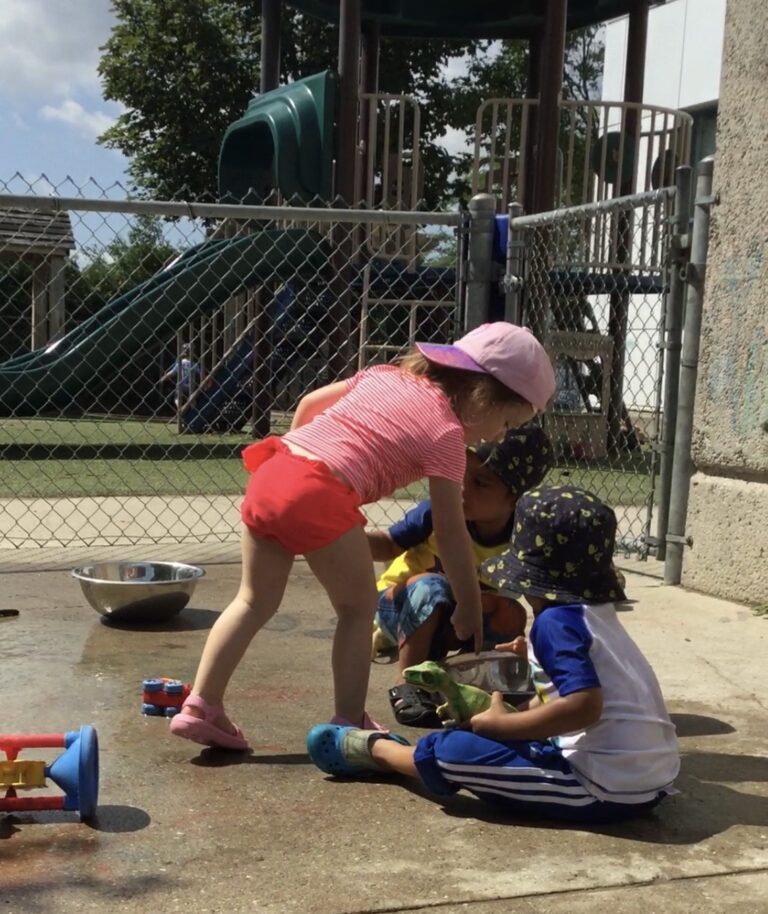 Three young children playing together on a wet concrete surface.