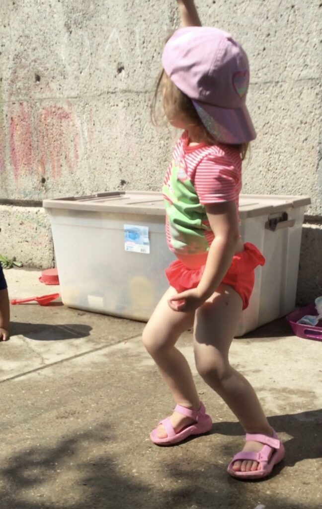 Child standing and raising her arm, after breaking ice during outdoor water play.