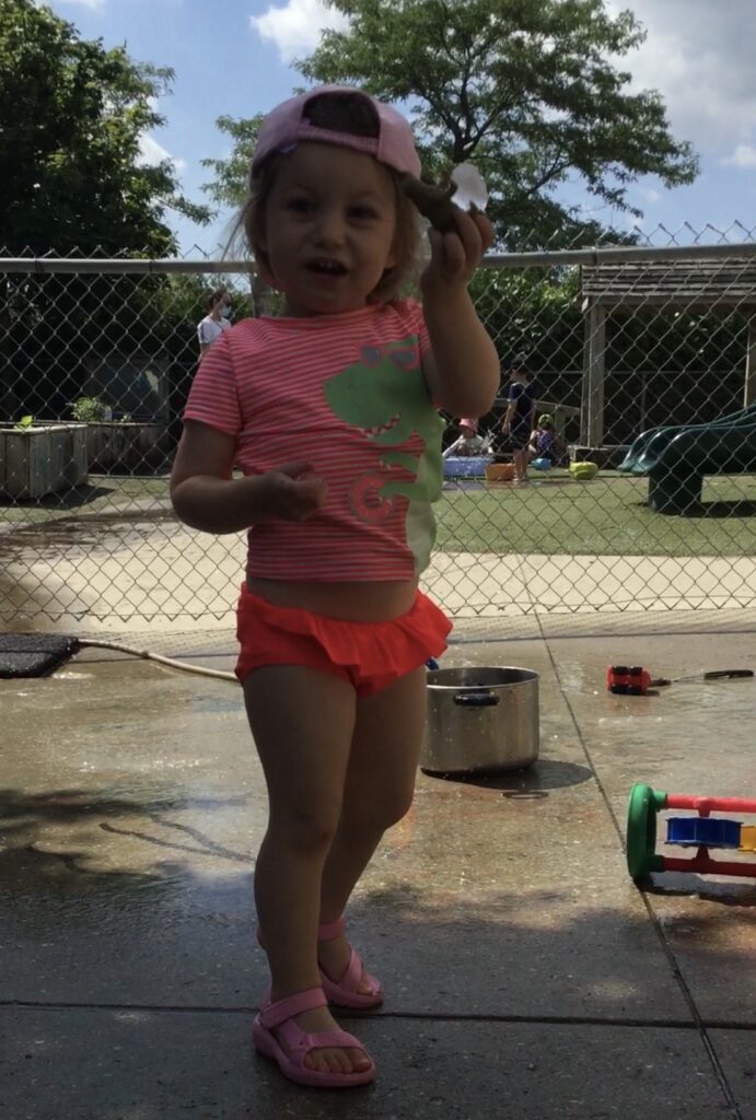 Young girl outdoors holding a chunk of ice with a toy animal inside, proudly showing it.