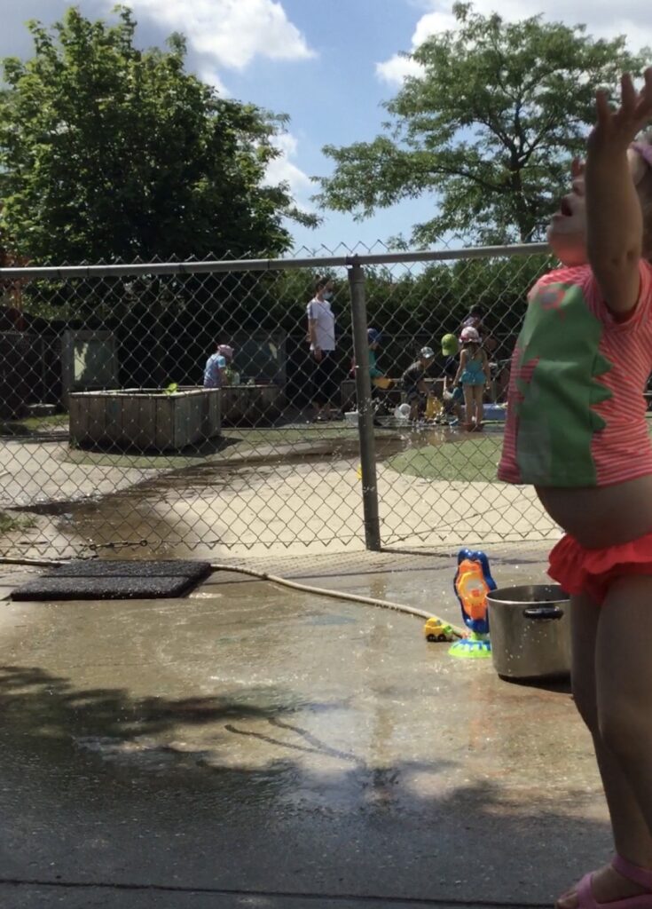 Child in swimsuit reaching upward, mid-motion while throwing ice during an outdoor activity.