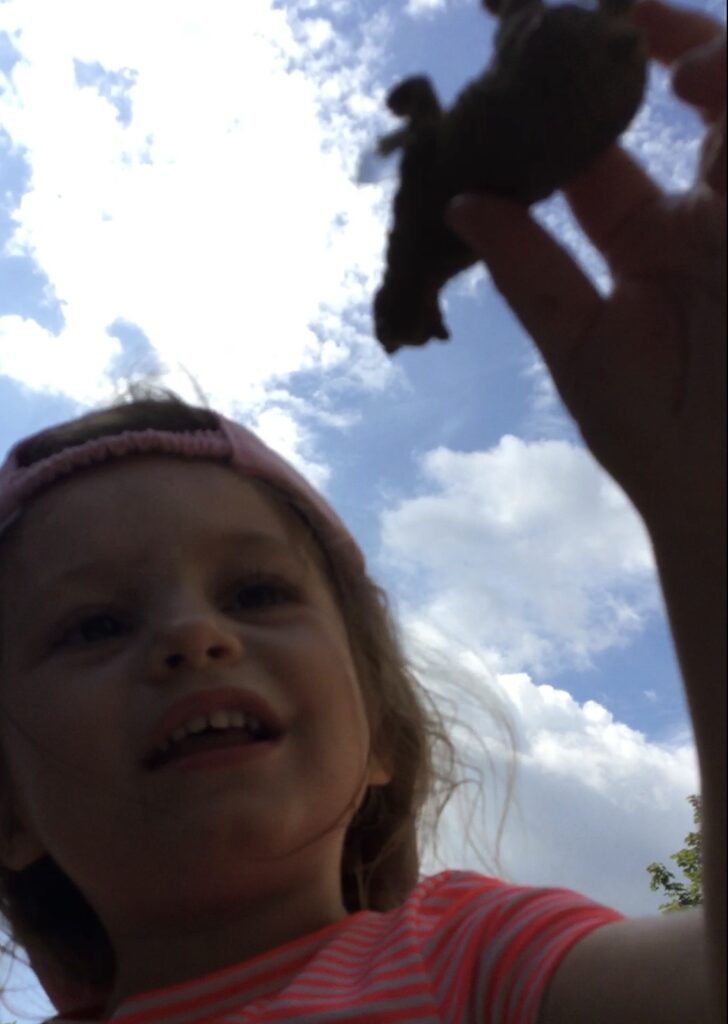 Close-up, low-angle shot of child holding up a dark animal figure against blue sky.