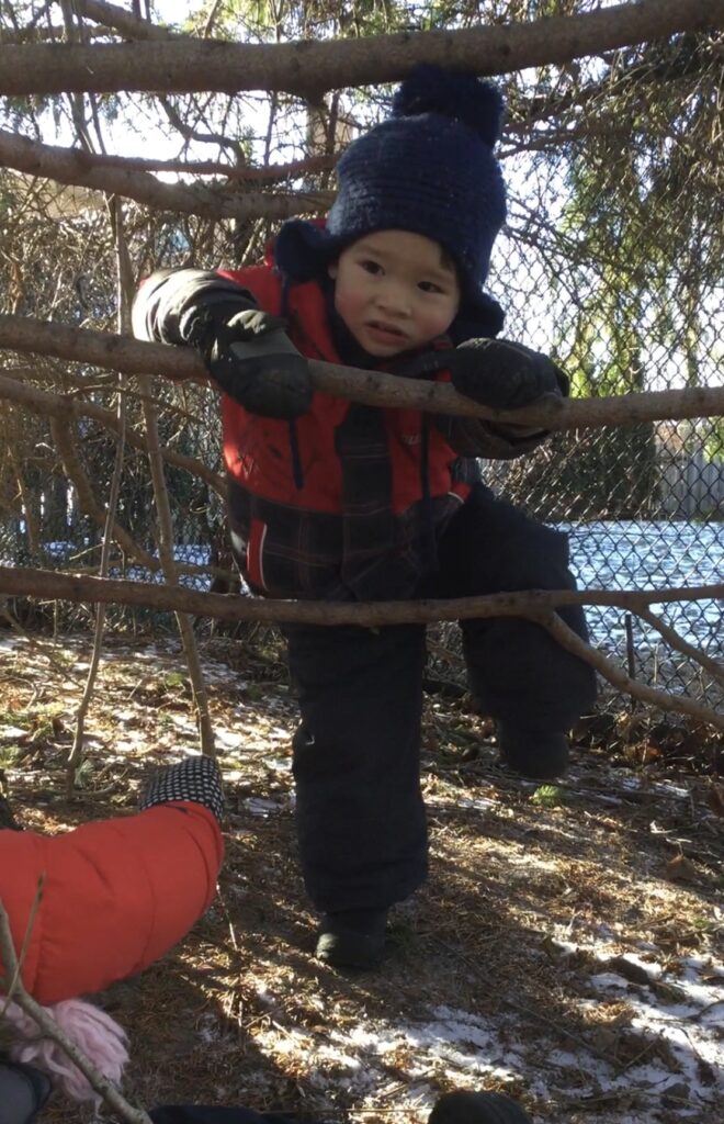 Toddler navigating through branches with determination during outdoor play.