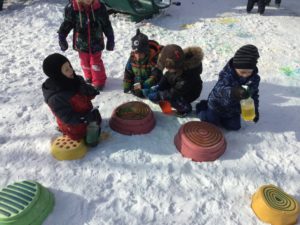 Children kneeling in the snow with coloured circular stumps.
