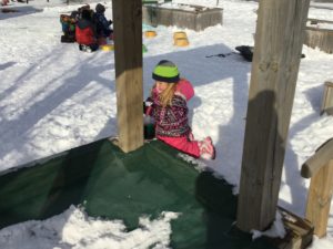 Child kneeling on a play structure, focused on spraying colour into the snow below.