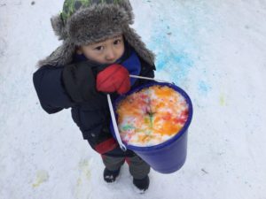 Child holding bucket filled with snow dyed vibrant colours.